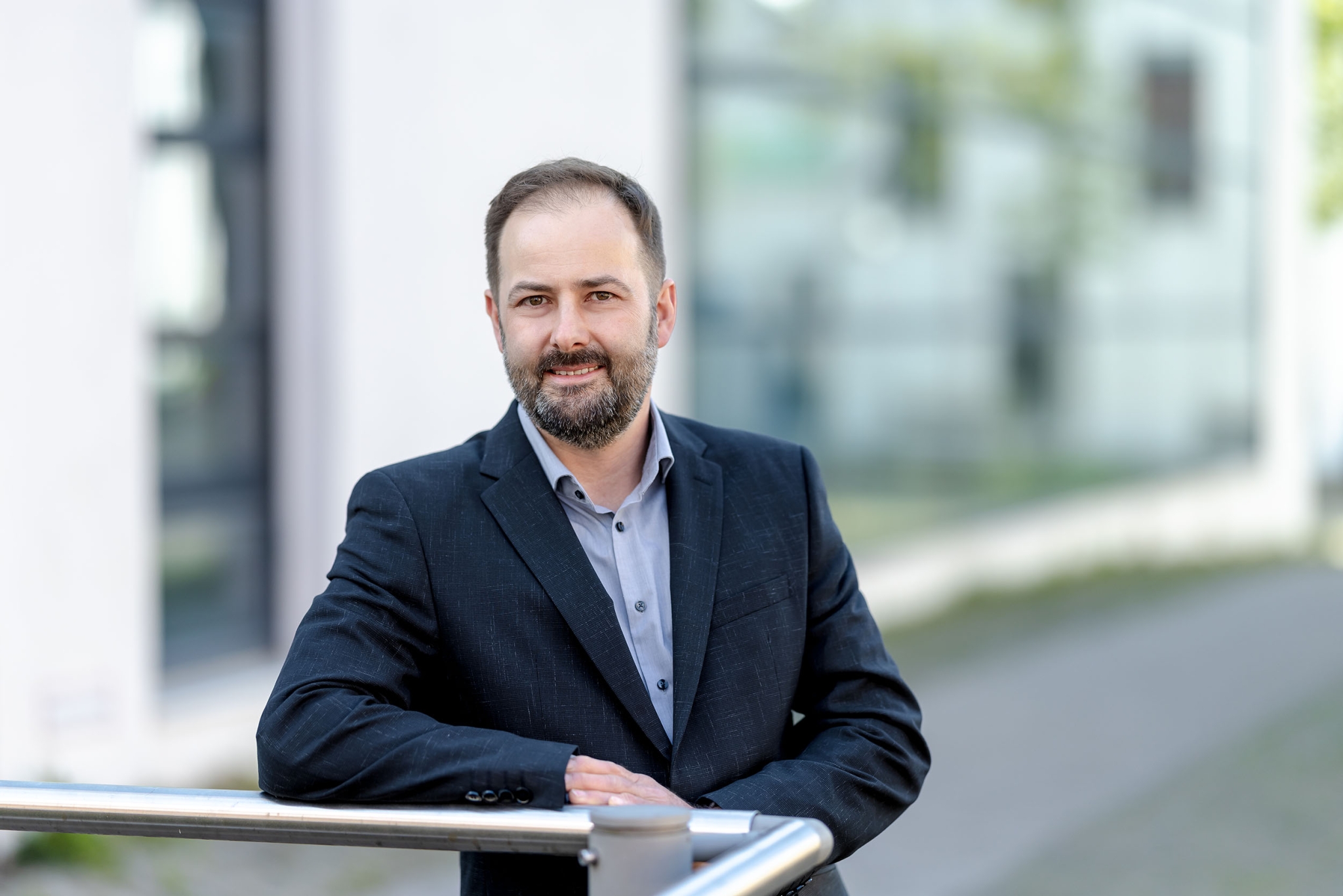 professionell & seriös im Business Look Sympathischer Geschäftsmann mit gepflegtem Bart und Anzug vor moderner Glasfassade, der selbstbewusst in die Kamera blickt fotografiert in Erfurt mit der EOS R 5MKII & dem RF 85mm f.12