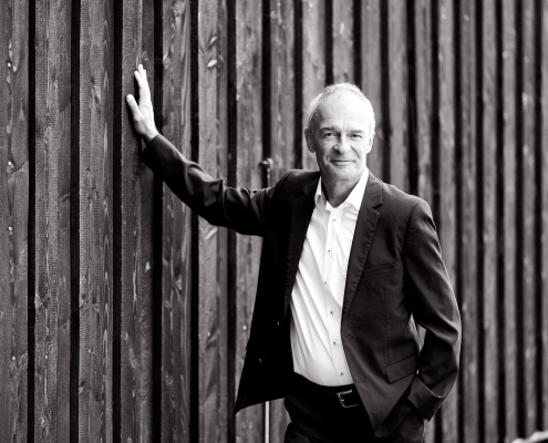 Zeitloses Business Porträt eines Mannes, der lässig an einer vertikalen Holzlattenwand lehnt fotografiert in Erfurt mit der Canon EOS R5MII & dem RF 135mm f1.8