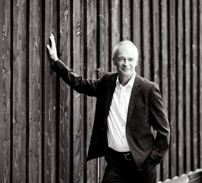 Schwarz-Weiß Porträt im Business Look Zeitloses Business Porträt eines Mannes, der lässig an einer vertikalen Holzlattenwand lehnt fotografiert in Erfurt mit der Canon EOS R5MII & dem RF 135mm f1.8