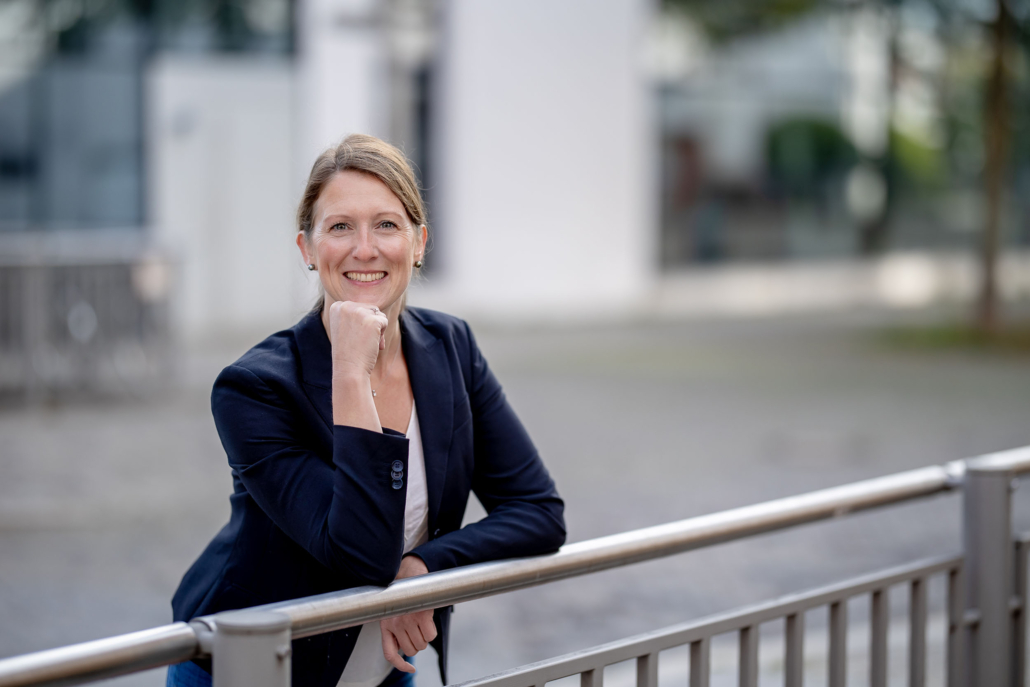 Porträt einer Geschäftsfrau Business Urban Sympathische Frau im Business-Outfit lehnt lächelnd an einem Geländer, im Hintergrund ein modernes Gebäude