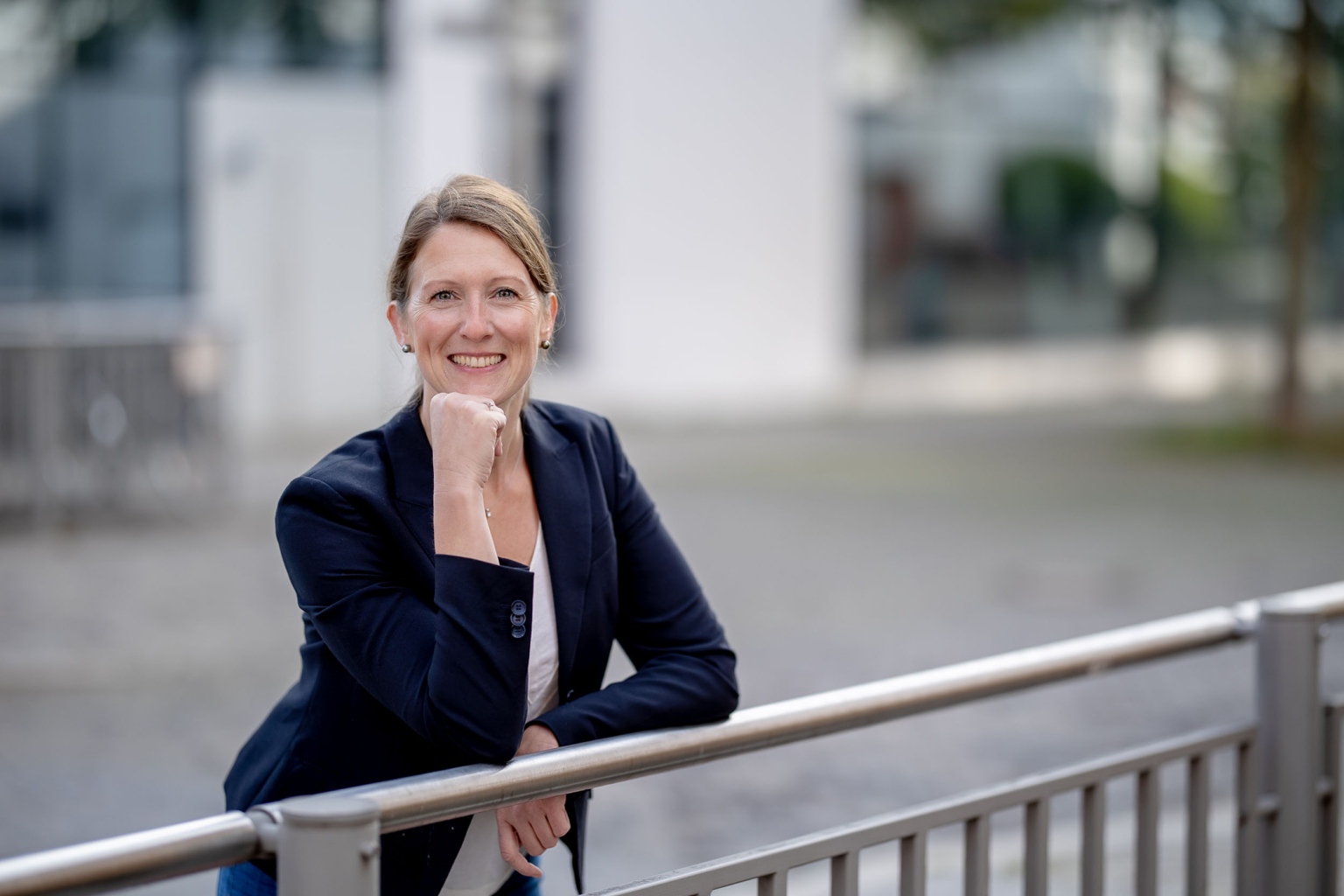 Porträt einer Geschäftsfrau Business Urban Sympathische Frau im Business-Outfit lehnt lächelnd an einem Geländer, im Hintergrund ein modernes Gebäude