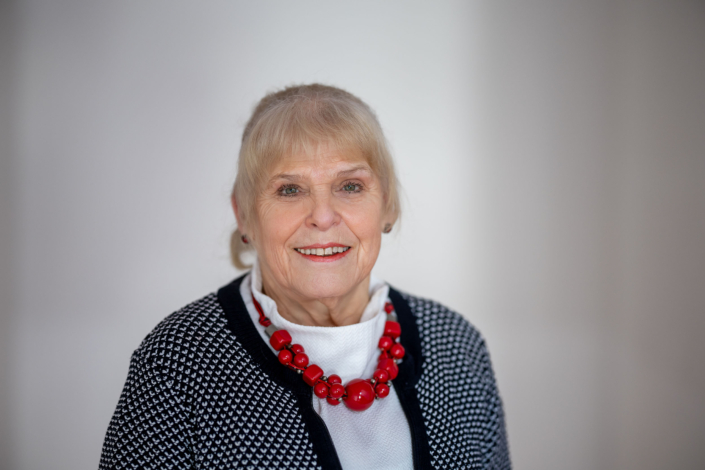 lächelndes Business Porträt Seniorin Porträt einer Seniorin in schwarz-weiß gemusterter Strickjacke mit roter Kette vor hellem Hintergrund