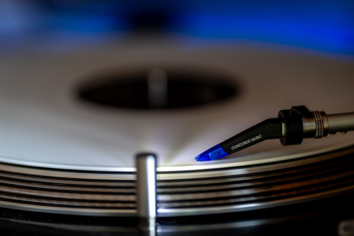 Ortofon Concorde Music Blue auf weißem Vinyl Nahaufnahme eines Ortofon Concorde Music Blue Tonabnehmers, der auf einer rotierenden weißen Vinylplatte auf einem Reloop RP 700MK2 aufliegt.