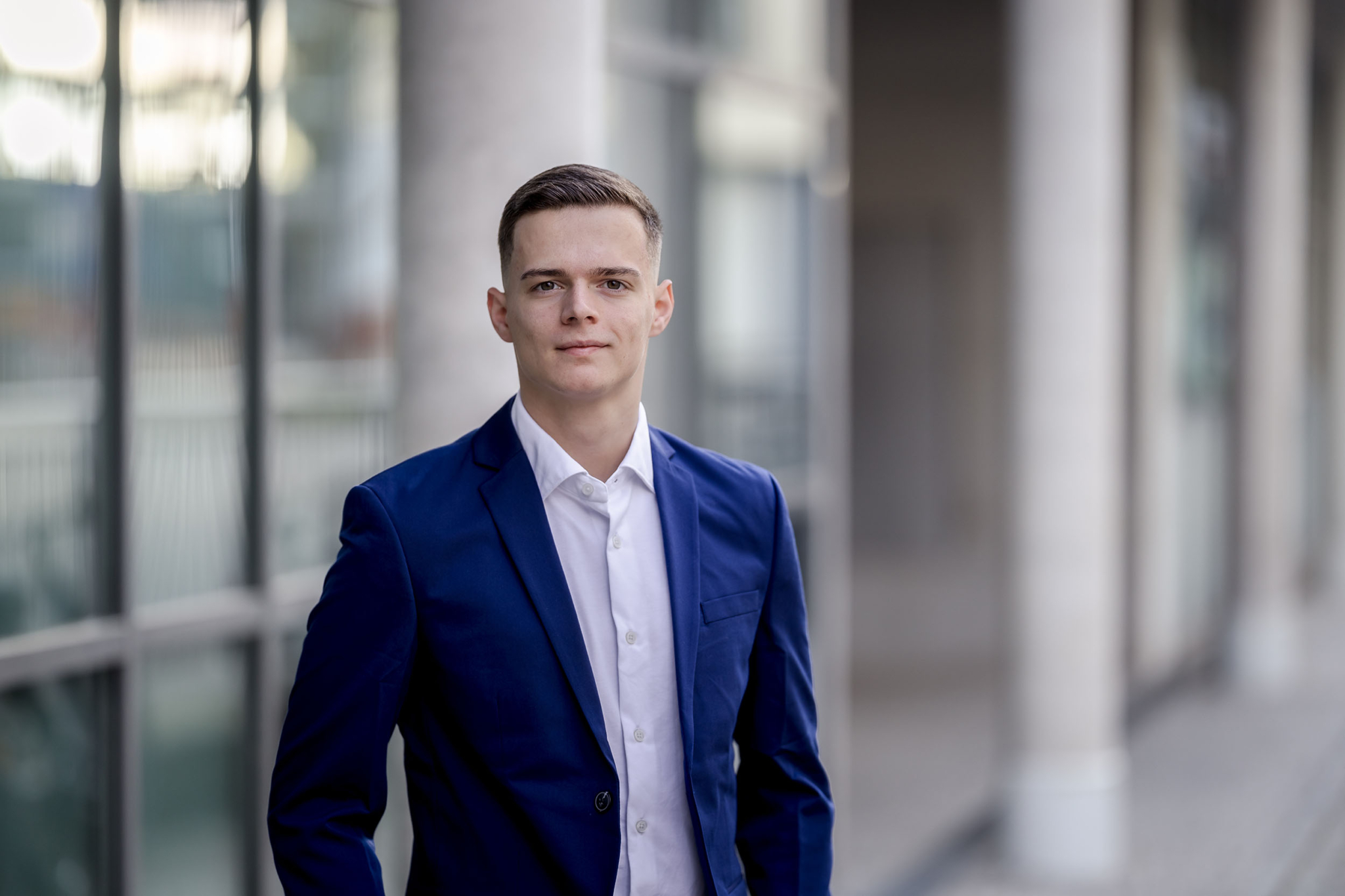 Corporate Porträt junger Mann in Erfurt Modernes Corporate Headshot eines jungen Geschäftsmanns vor einer hellen Glasfassade mit weichem Bokeh im Hintergrund.