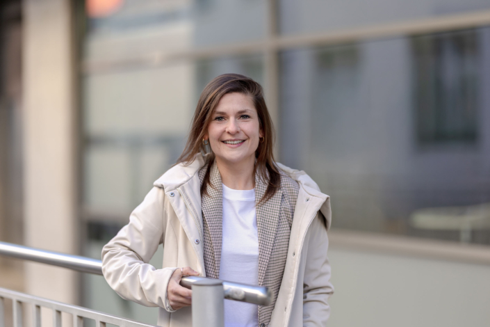 Business Casual Look Modernes Umfeld Businessporträt einer Frau im Layering-Outfit aus Shirt, Karoblazer und Jacke vor moderner Architektur. Equipment: Canon EOS R5M² & RF 85mm f1.2.