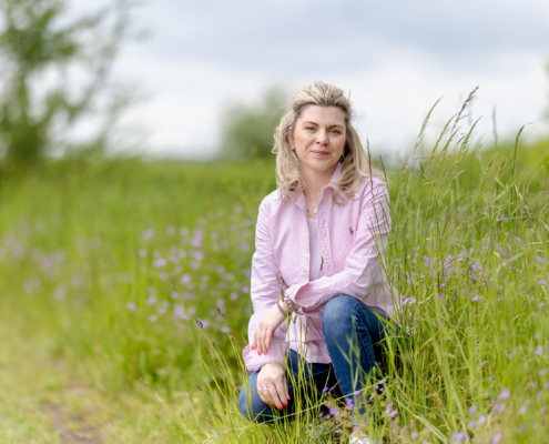 Professionelles Porträt einer Frau in einer sommerlichen Wiese sitzend