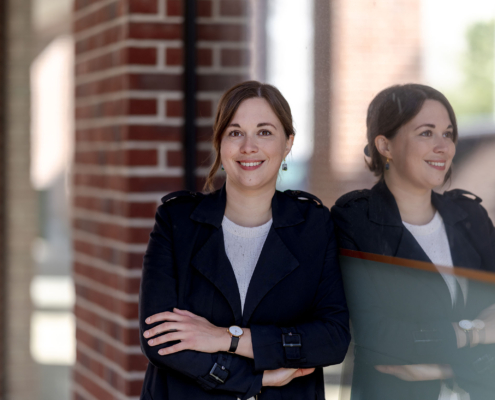 Business-Foto mit Reflexion Authentisches Business-Porträt einer lächelnden Frau im dunklen Trenchcoat und weißem Pullover