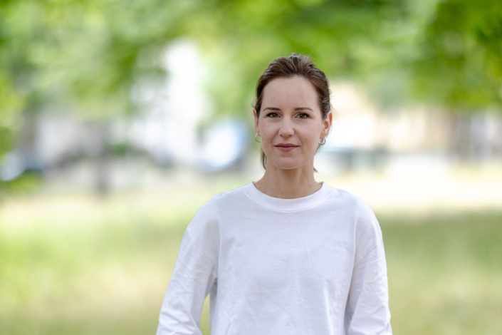 Pur und Echt: Die Kunst der Reduktion im Porträt Ein cleanes und ruhiges Porträt einer Frau mit hochgestecktem Haar, das durch seine schlichte Komposition und das weiche grüne Bokeh wirkt.