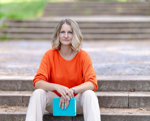 Businessportrait im Park Natürliches Porträtfoto einer Frau im Freien, die auf einer Treppe sitzt und ein Notizbuch hält,